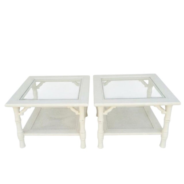 A pair of vintage Mersman white faux bamboo and cane side tables. The tables feature glass tops with faux bamboo details...