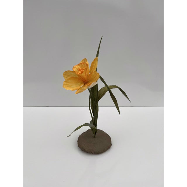 This artwork features a delicately crafted flower emerging from a textured cement base, showcasing a harmonious blend of...
