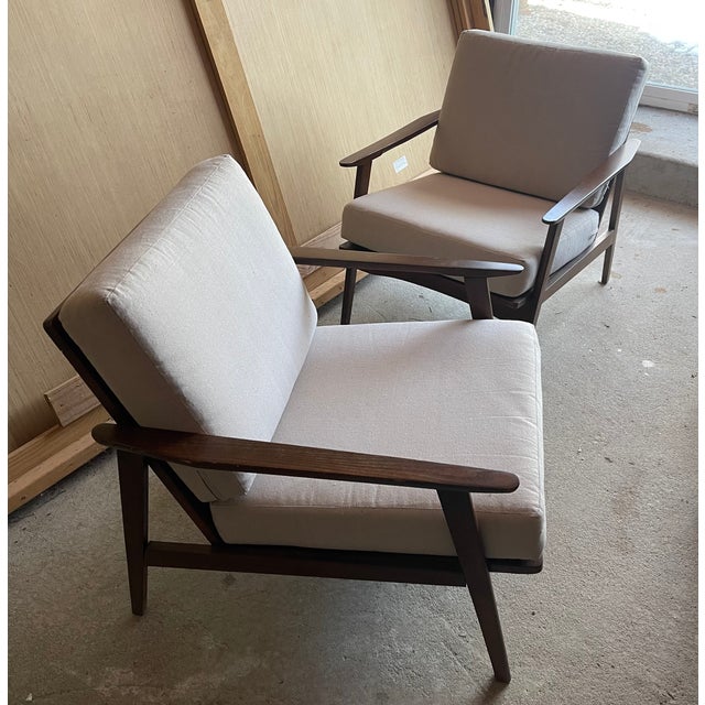 A striking pair of mid-century modern lounge chairs featuring a solid wood frame with beautifully sculpted arms and...
