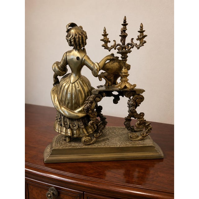 Intricately detailed vintage brass Rococo figural sculpture featuring a Victorian woman beside an ornate candelabra and...