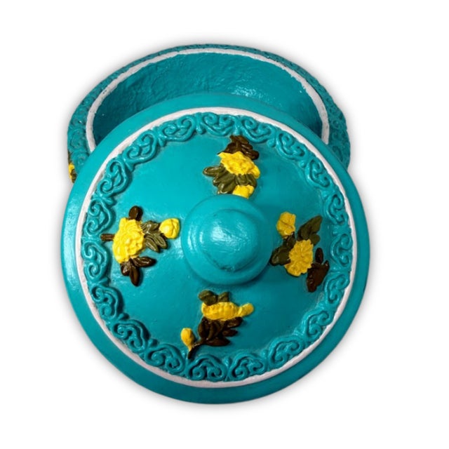 Vintage-style round trinket box features a vibrant turquoise blue finish with intricately raised yellow floral accents....