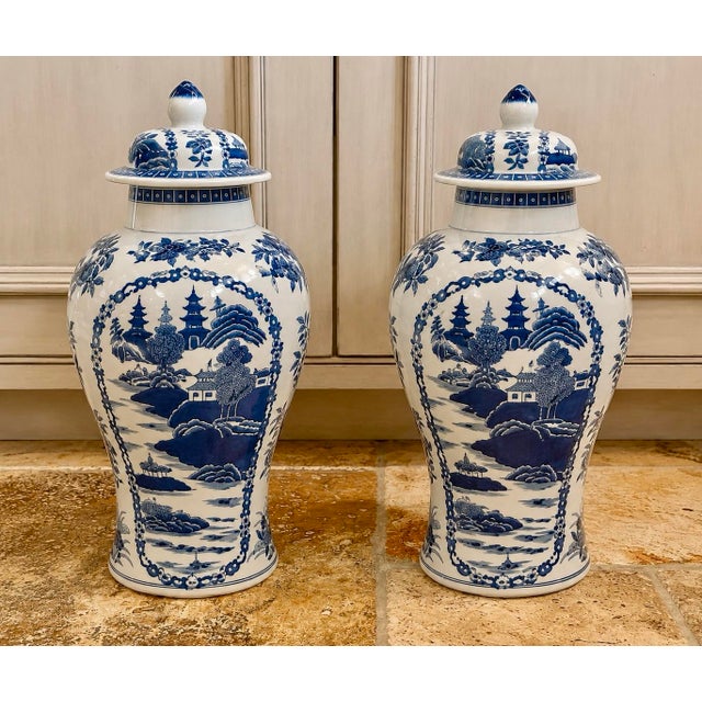 Elegant pair of blue and white chinoiserie porcelain ginger jars with matching lids, featuring richly detailed landscape...