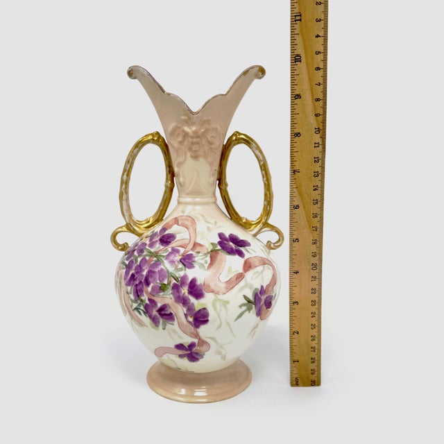 Up for sale is a beautiful vintage porcelain vase featuring a delicate hand-painted purple floral motif wrapped in pink...