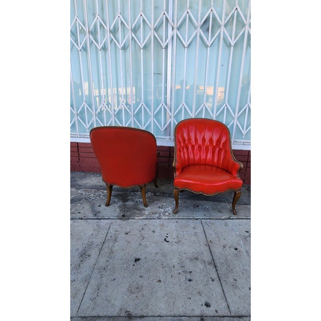 Vintage-style armchairs with red leather upholstery. Each chair has a tufted backrest and seat with decorative nailhead...