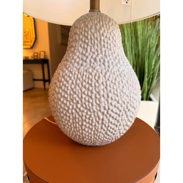 Contemporary table lamp featuring a sculptural textured ceramic base with an organic pebble-inspired design that adds...