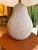 Contemporary table lamp featuring a sculptural textured ceramic base with an organic pebble-inspired design that adds...