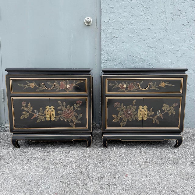 Elegant pair of vintage Cantonese nightstands featuring glossy black lacquer finishes accented with hand-painted floral,...
