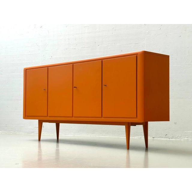 An exceptionally striking, large-format sideboard from the 1960s in a vibrant orange. The clean, strictly structured front...