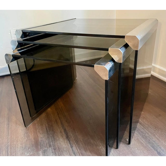 A modern set of three nesting tables in chrome metal and smoked glass by Pierangelo Gallotti. It has all the Classic...
