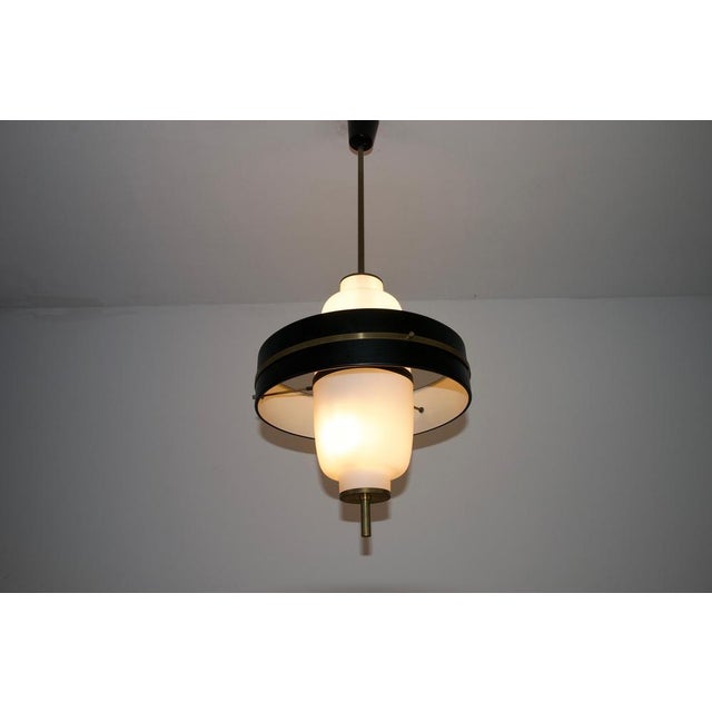 This italian pendant lamp from the 1960s is a refined example of mid-century lighting, combining brass, opal glass, and...