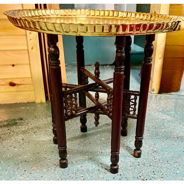 This elegant piece features an intricately engraved circular brass tray resting atop a folding dark wooden stand. It...