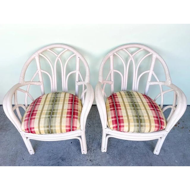 Presented by Palm Beach Regency, a pair of vintage rattan armchairs with upholstered seats. All pieces are sold in nice as...