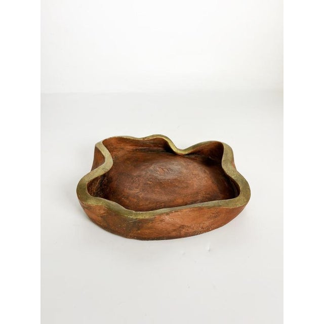 Sculptural ceramic ashtray with an organic freeform silhouette and warm terracotta-toned glaze, accented by an irregular...