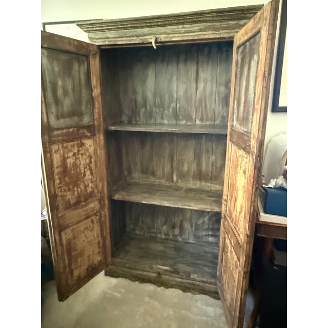 A tall, two-door wooden armoire featuring a distressed dark finish and multi-paneled cabinet doors. The upper cornice is...