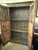 A tall, two-door wooden armoire featuring a distressed dark finish and multi-paneled cabinet doors. The upper cornice is...