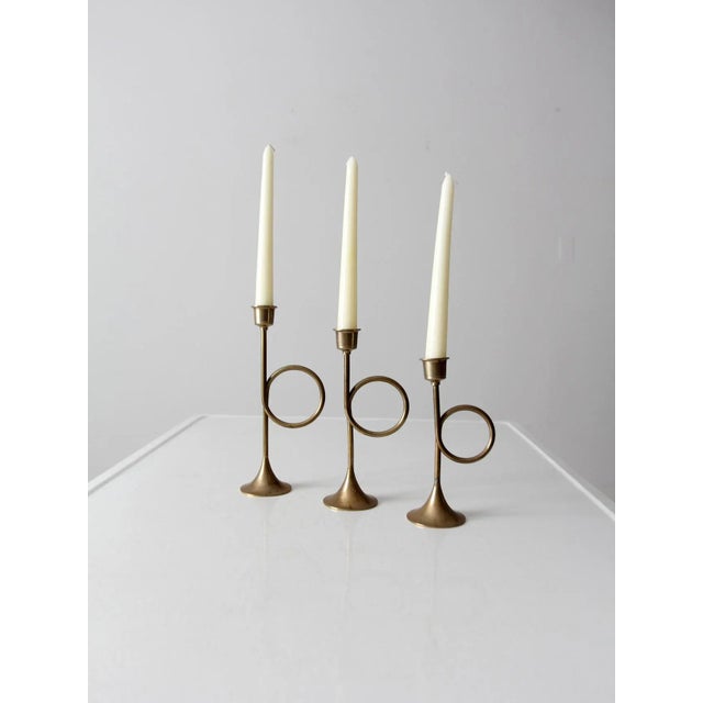 A collection of mid-century brass candle holders shaped as bugle trumpets, each varying in size to create a balanced,...
