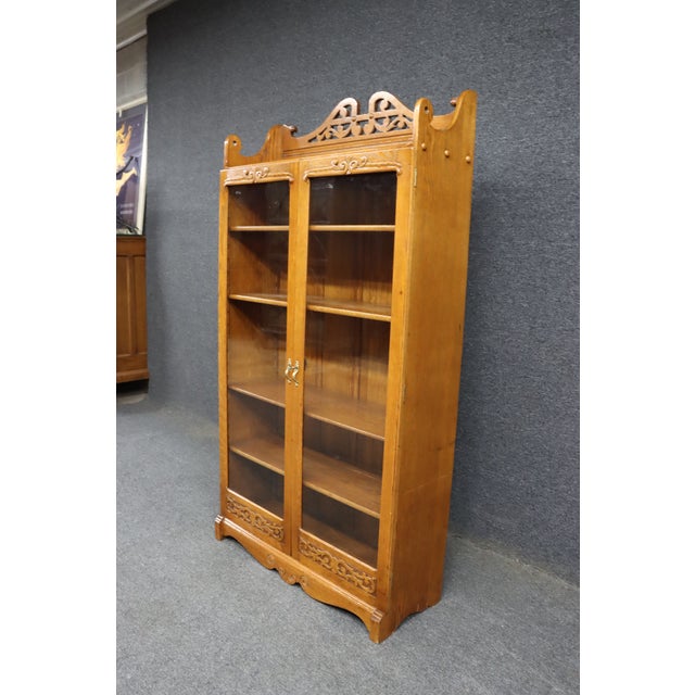 Victorian two-door oak bookcase featuring a pierced gallery crest, carved scroll detailing, and full-length glazed doors....