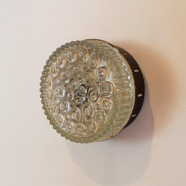 Vintage 1970s round wall lamp with a textured glass shade. It emits a warm, ambient light and creates an elegant focal...