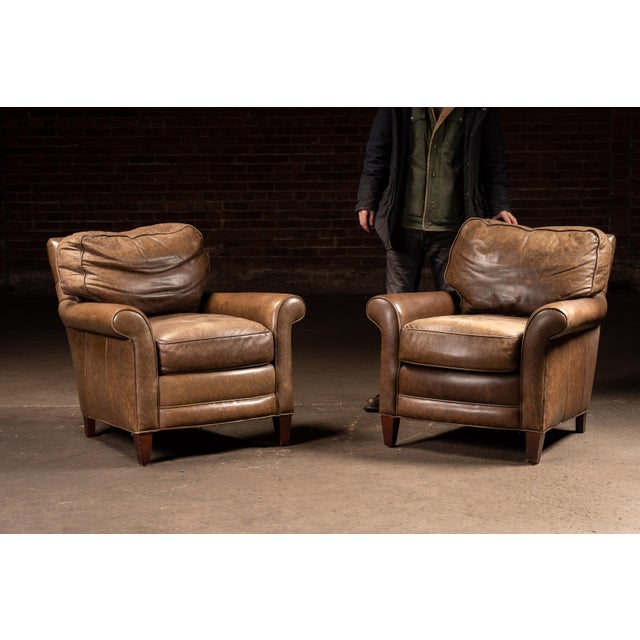 Matching pair of leather club chairs with a relaxed, overstuffed profile and gently rolled arms. Each chair features a...