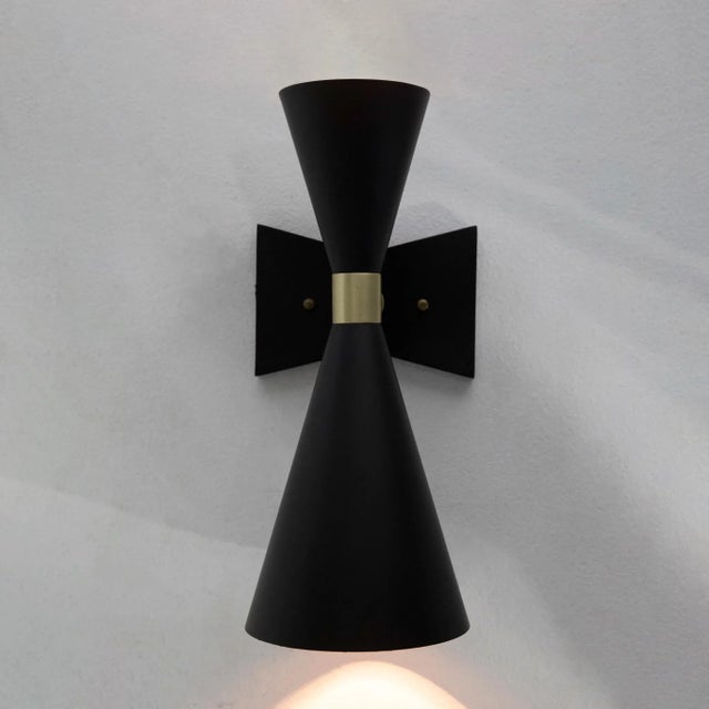 A crimp of champagne metal connects the two cones that make up the artisan crafted Ariel Sconce.