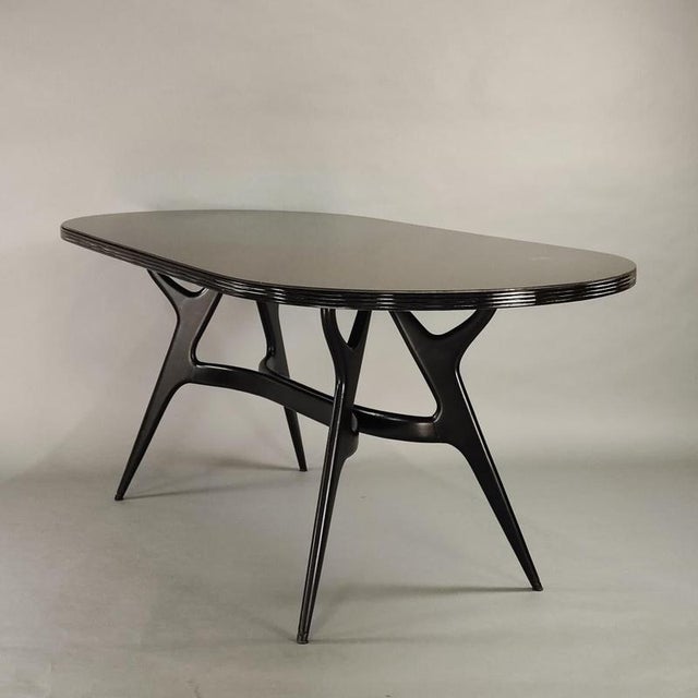 1950s design. Frame with black lacquered wooden legs, oval chocolate-colored glass top. Can be replaced with new glass in...