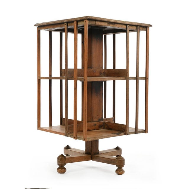 An elegant antique English rotating bookcase in wood, square in shape, resting on a central pivoting base allowing easy...