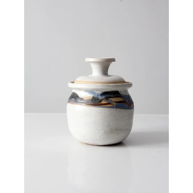 This is a vintage studio pottery jar. Signed by the artist, the hand-crafted pottery jar features a soft white glaze with...