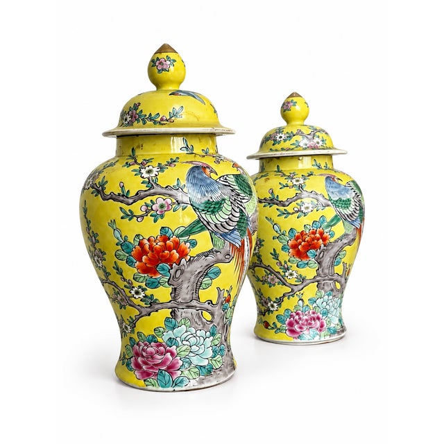 A vivid matching pair of lidded ginger jars with sunny yellow grounds and richly colored birds, flowering branches, and...