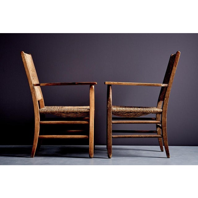 A pair of rustic armchairs with solid oak frames and hand-woven rush seats and backs, exemplifying vernacular...