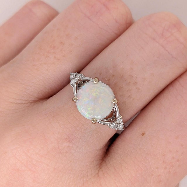 An Australian opal glows in a shifting play of colour at the centre of this solid 14K white gold ring, encircled by six...