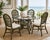 A beautifully sculpted 5-piece rattan dining set by Ritana, featuring a round glass-top table and four coordinating cane-...