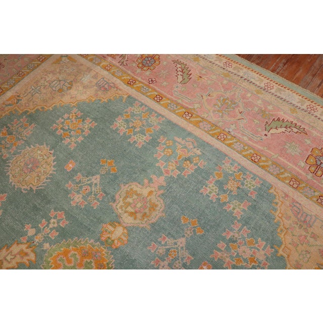 A colorful antique early 20th century Turkish Oushak rug. The field is teal; the border is pink. The rug has a lot of...