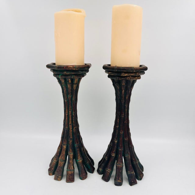 A pair of tall, heavy bronze-finish metal bamboo pillar candleholders. The design mimics clustered bamboo stalks flaring...