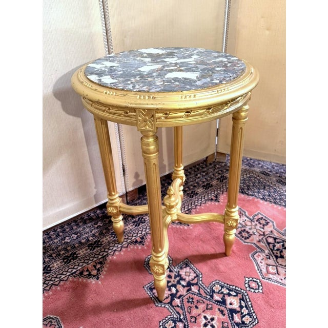 A round, giltwood pedestal table in the Louis XVI style, circa 1880. Made of carved wood with a veined white marble top....