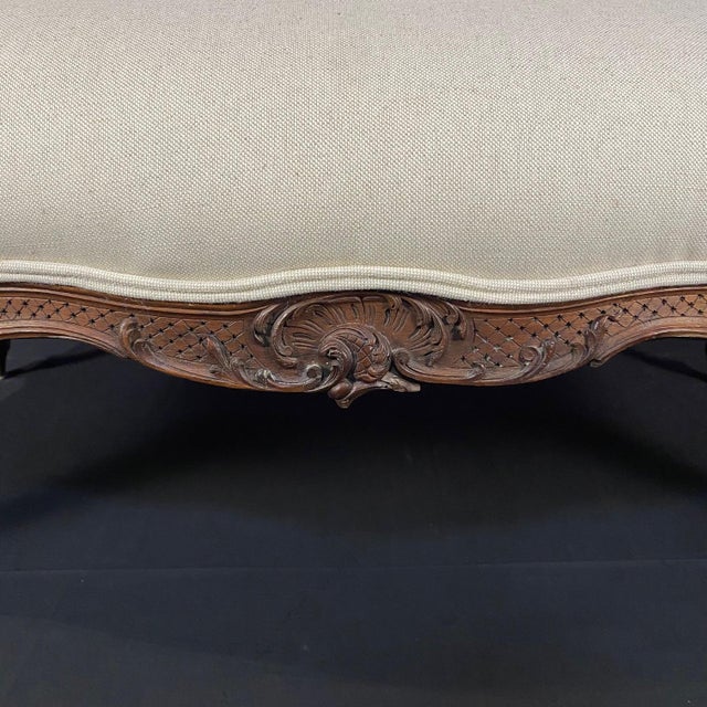 A Louis XV-style intricately carved walnut sofa with shaped upholstered backrest, which leads to scrolled partially...