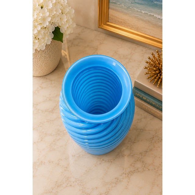 A striking vintage sculptural art glass vase featuring an elegant ribbed swirl design in a vibrant sky-blue hue. Its...