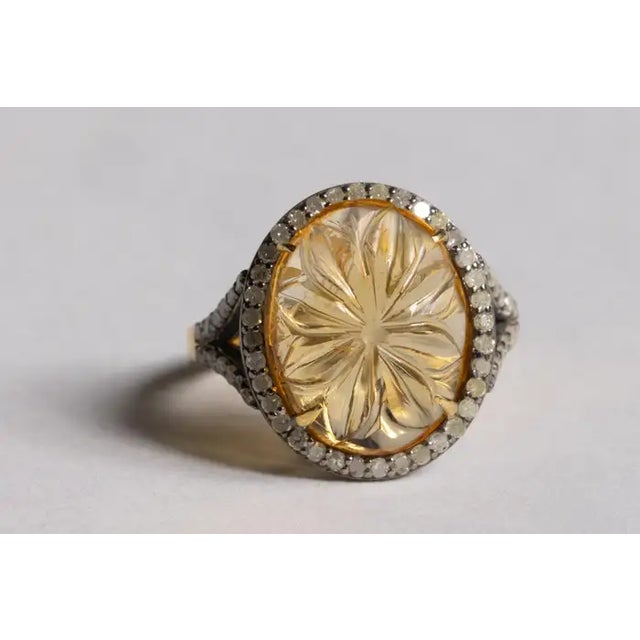 A carved oval citrine gemstone with a flower design, bordered with round, pave`-set diamonds. Set in an oxidized sterling...