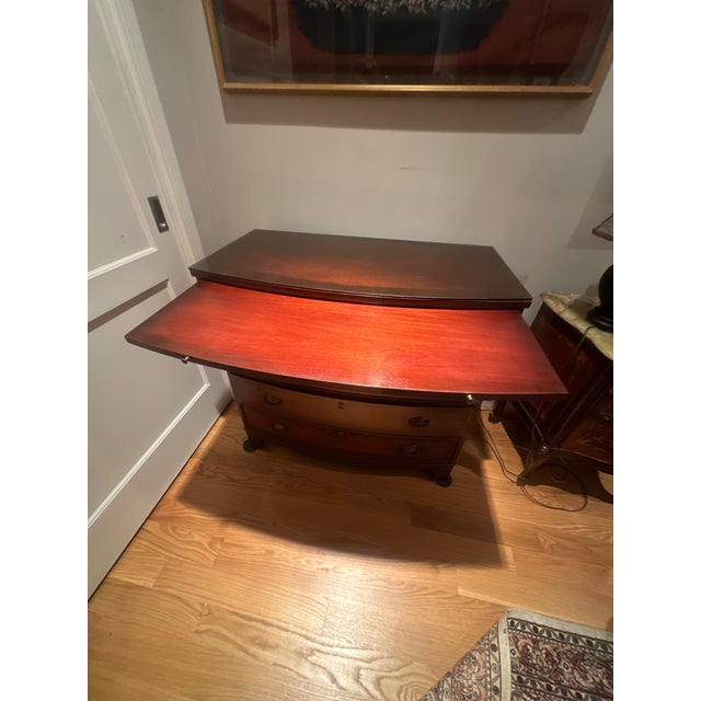 This is a mahogany bowfront chest of drawers with a pull out writing shelf. A glass top covers the surface. There are...