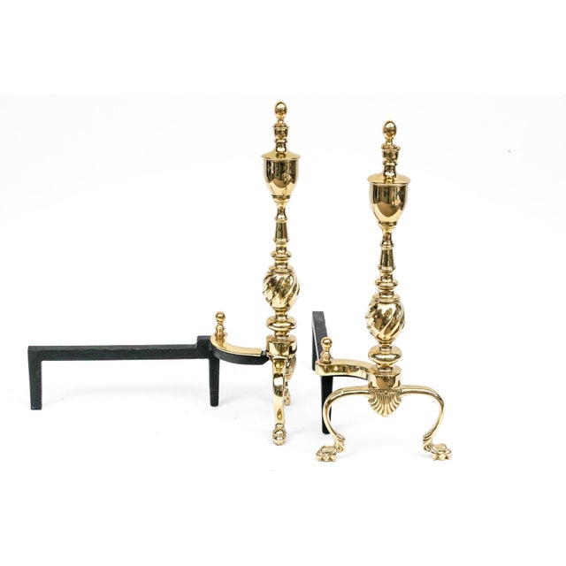 A pair of Georgian style polished brass andirons with tall urn-form, ball-topped finials, twisted central sphere, shell-...