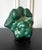 A malachite rock specimen with intense green and black colors fitted on a wood stand. The gemstone in the botryoidal form...