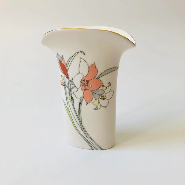 A 1980s vintage vase with a glossy white finish and floral lily design. Gold trim around the opening and fluted shape....