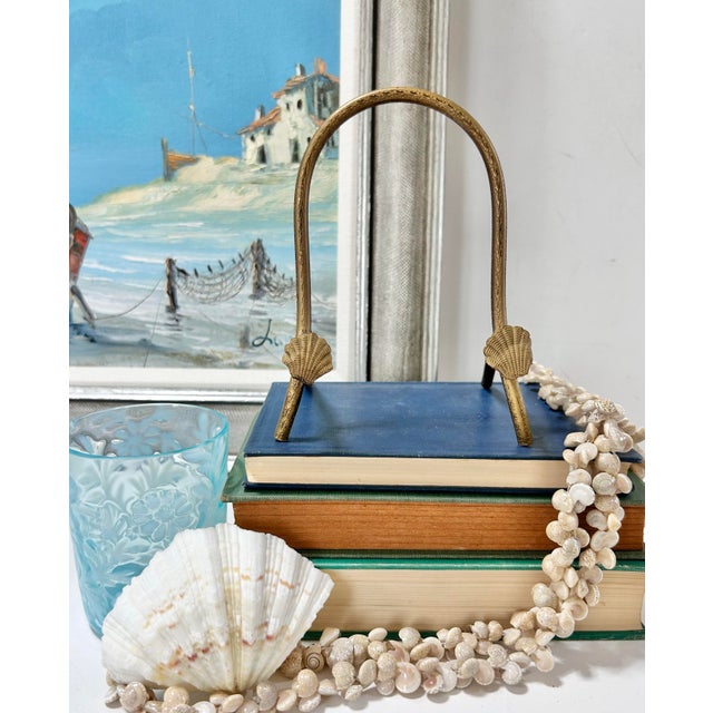 Vintage brass display stand featuring sculptural shell accents and an arched silhouette, offering a refined coastal...