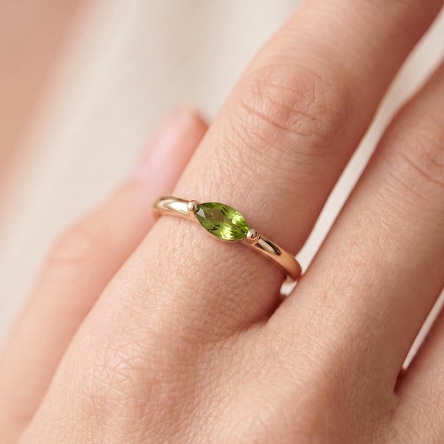A fresh, minimalist solitaire featuring a vibrant green marquise-cut peridot set in an east-west orientation, held by a...