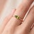 A fresh, minimalist solitaire featuring a vibrant green marquise-cut peridot set in an east-west orientation, held by a...