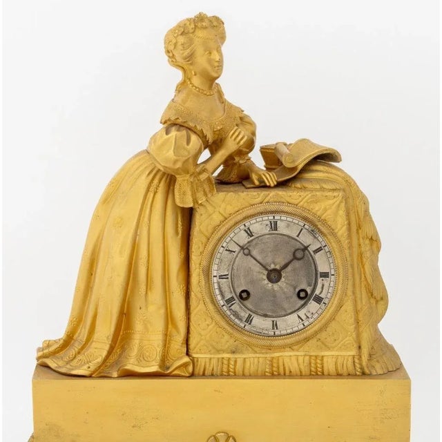 French Empire Gilt Metal Figural Clock, circa 1830, the circular dial with strike on bell movement, surmounted by a woman...
