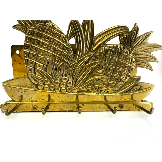 A striking vintage brass wall rack featuring a bold pineapple and foliage motif, rendered in richly textured relief with a...