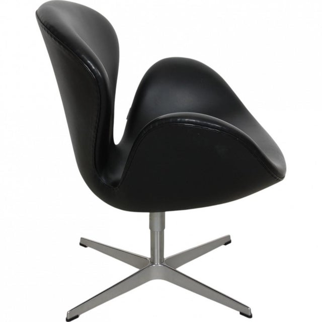 Arne Jacobsen Swan chair upholstered with original black Aura leather, and with a brushed aluminium swivel base. The chair...