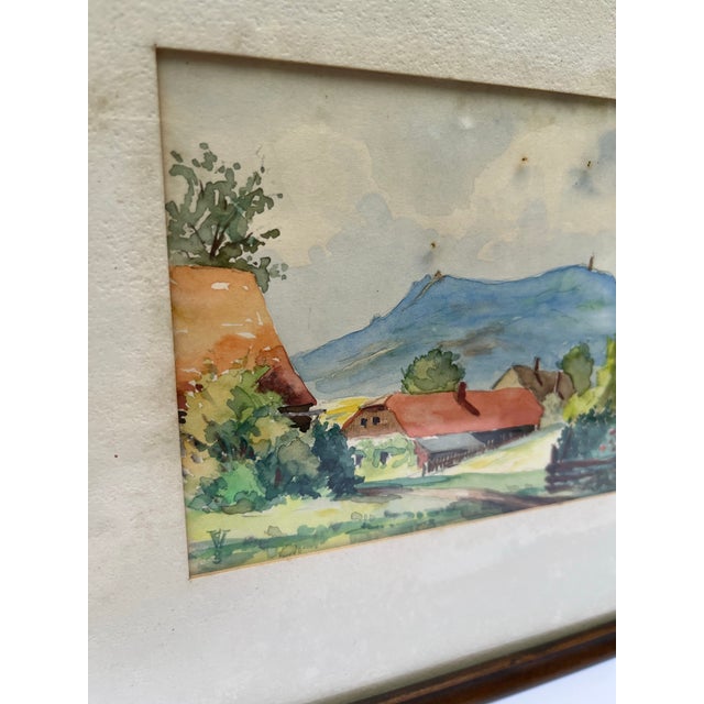 A small original plein air style watercolor painting of a building in a landscape. Finished with glass and wood frame.