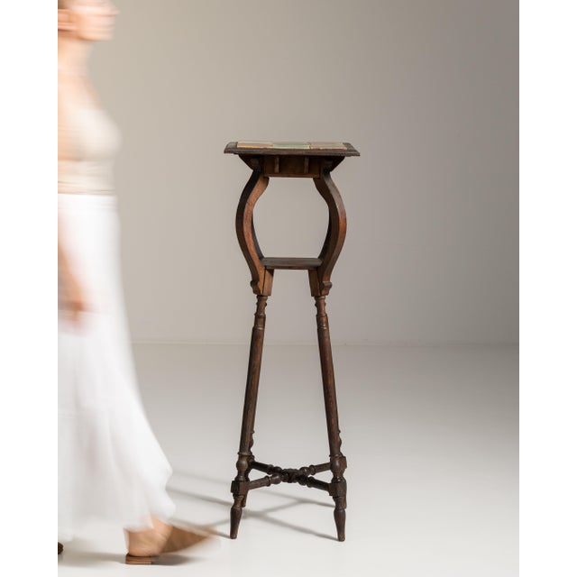 This 1910s Art Nouveau pedestal table with ceramic tile top from France is made in dark wood as a tall, slender stand on...