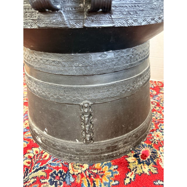 A striking metal drum table featuring a broad circular top with finely incised concentric decoration and figural frog-form...